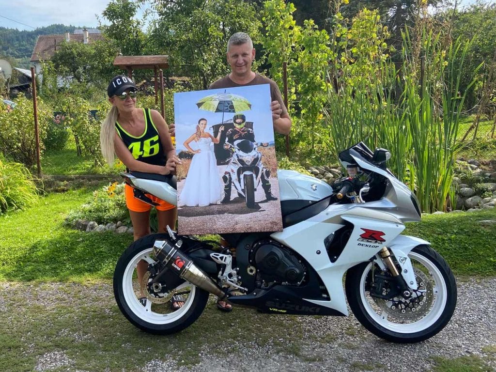 Pár drží svadobnú fotografiu vytlačenú na plátne pri bielej motorke