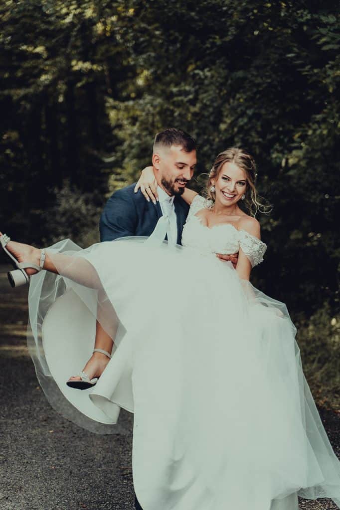Ženích nesie nevestu na rukách po lesnej ceste, obaja sa smejú
