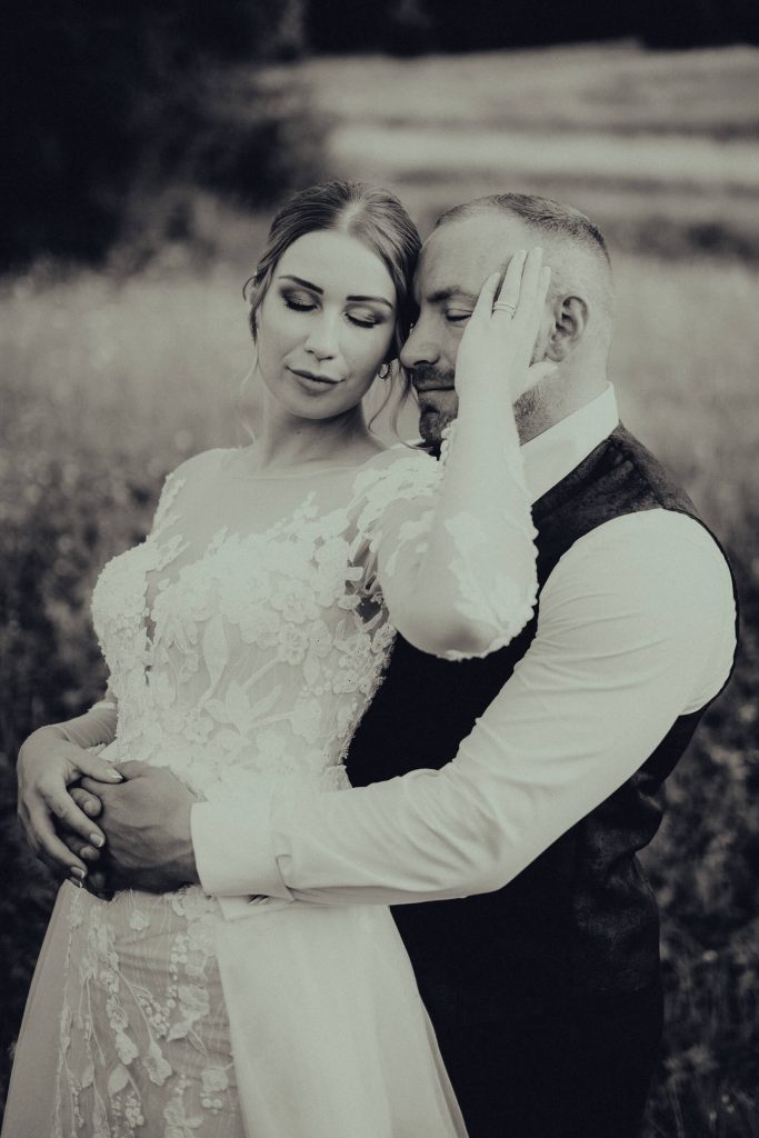 Ženích objíma nevestu so zatvorenými očami, čiernobiely záber na lúke