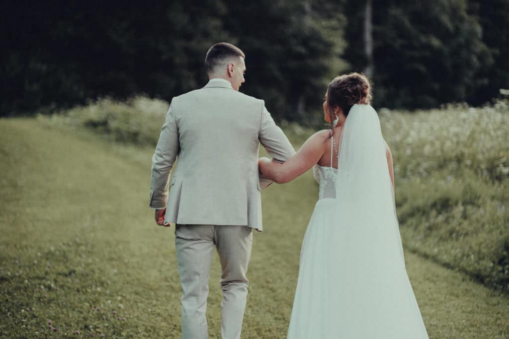 Nevesta a ženích kráčajú zozadu po trávnatom chodníku k lesu