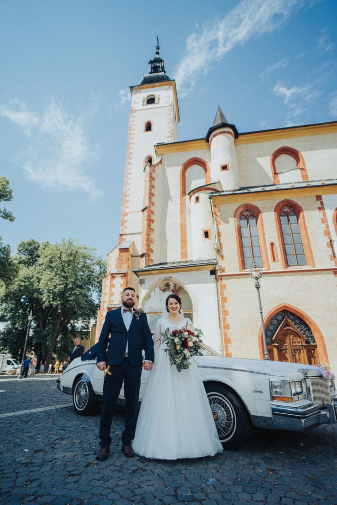 Pár pri bielej veteránskej limuzíne pred kostolom v Banskej Bystrici