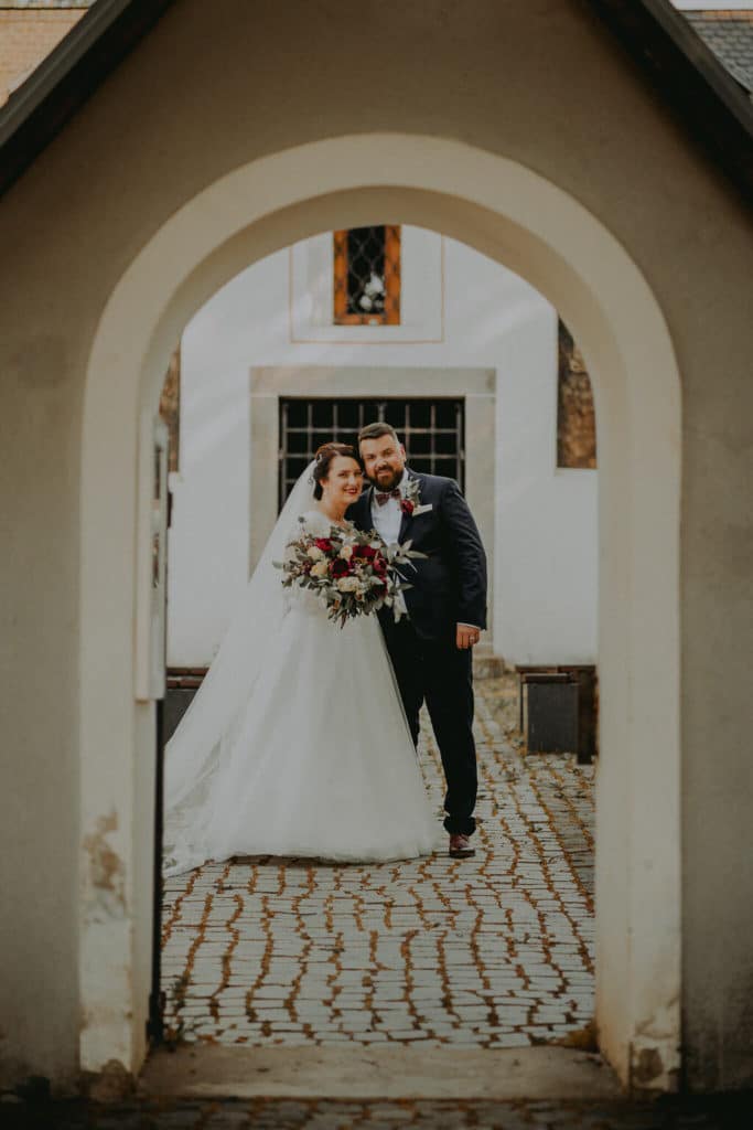 Andrea a Peter prechádzajú klenutou bránou na dláždené nádvorie