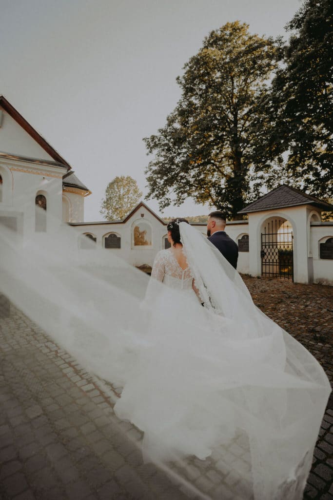 Nevesta s dlhým závojom na chodníku pred bielym kostolom