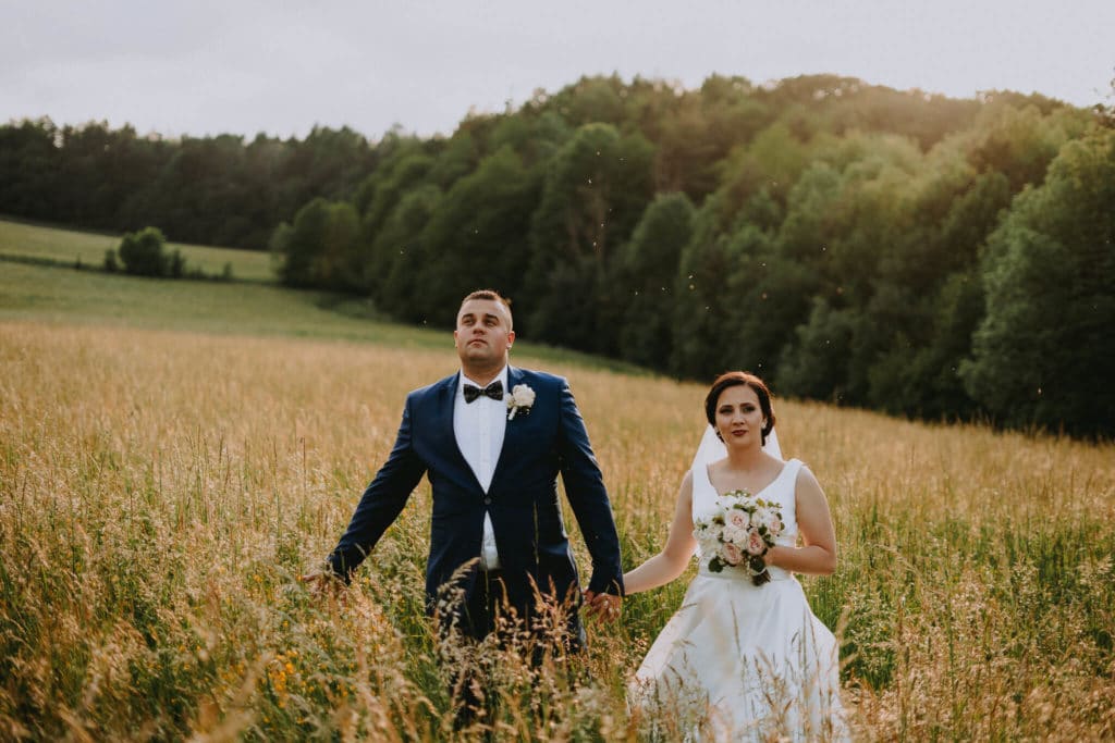 Peťka a Maťo kráčajú k fotografovi cez vysokú trávu pod zeleným lesom