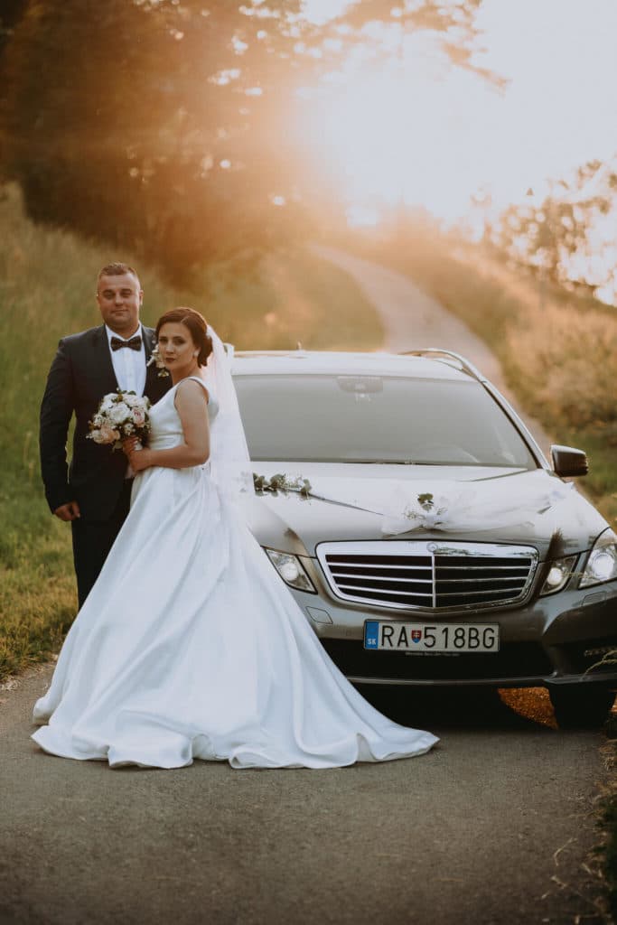 Peťka a Maťo pri striebornom mercedese s kvetinovou výzdobou na ceste