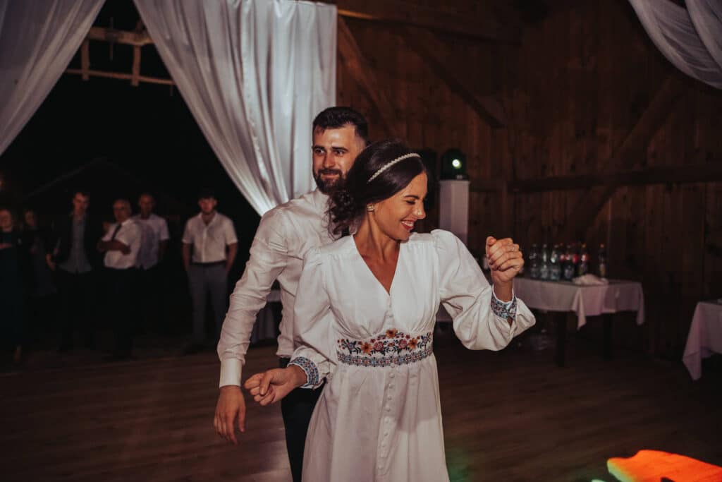Adriana v bielych šatách s ľudovou výšivkou tancuje s partnerom v stodole