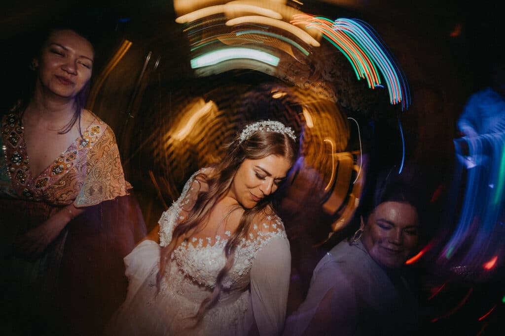 Nevesta tancuje s hosťami medzi rozmazanými farebnými svetlami na zábave