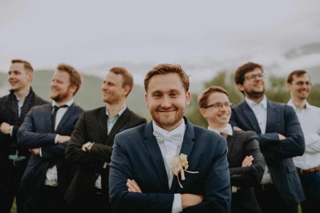 Usmiaty ženích so skríženými rukami pred skupinou svojich priateľov
